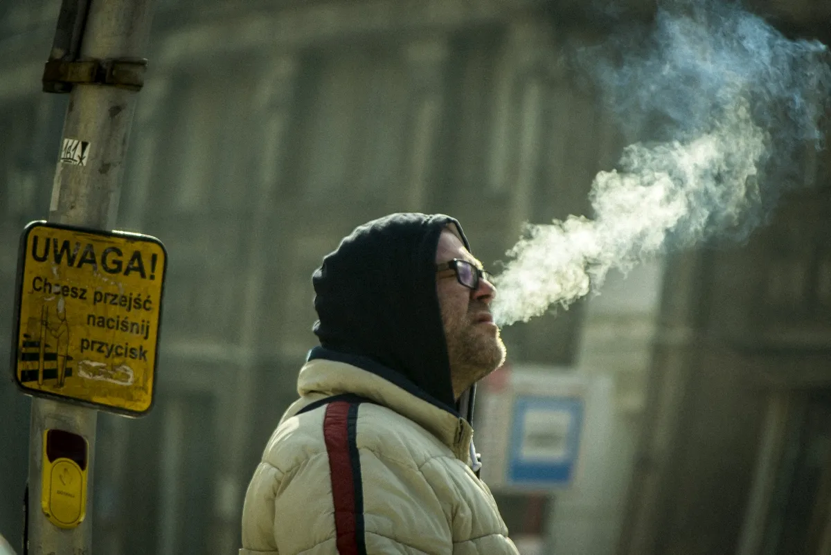 Hooded smoker exhaling into the cold air beside a yellow sign